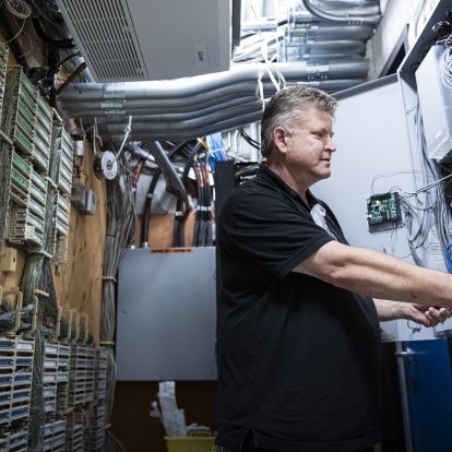 Andrew Schick is photographed working on equipment at the Kingston General Hospital site. He has short, salt and pepper hair, blue eyes and is wearing a black polo shirt.