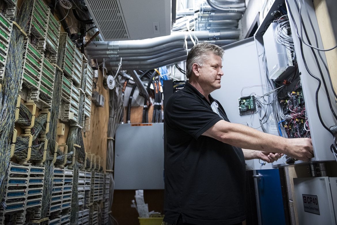 Andrew Schick is photographed working on equipment at the Kingston General Hospital site. He has short, salt and pepper hair, blue eyes and is wearing a black polo shirt.