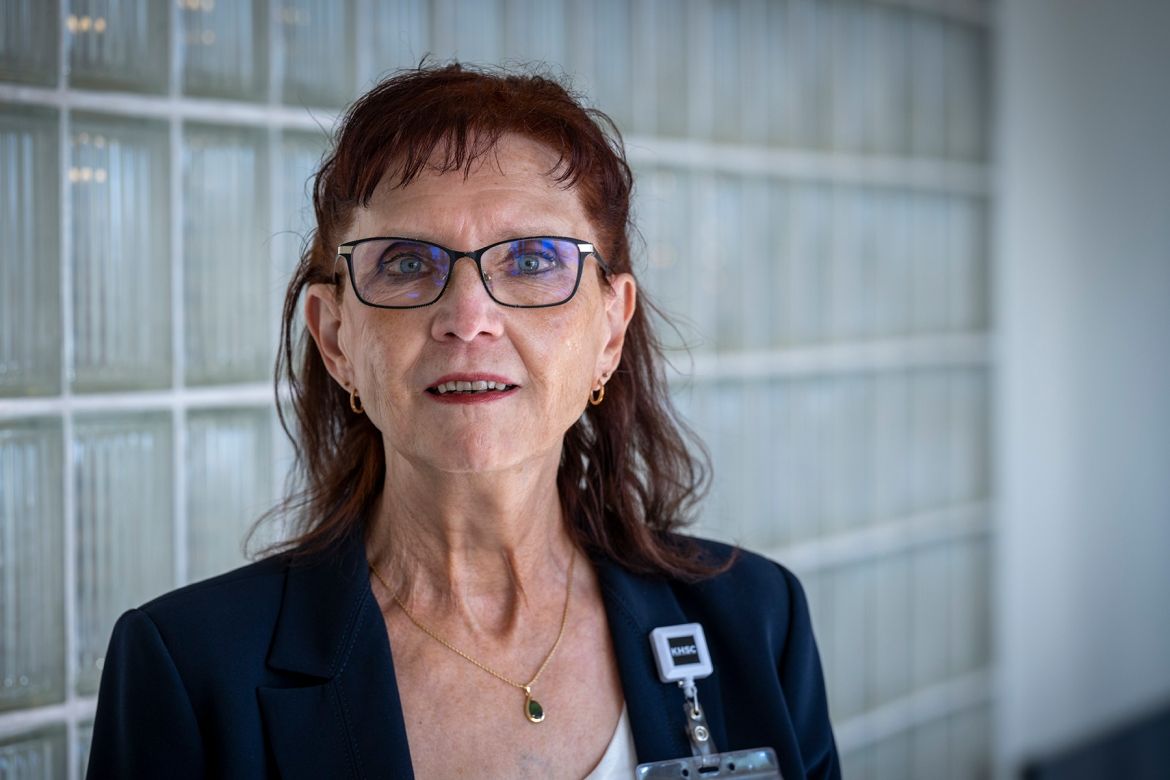 Margaret Bollen is pictured standing in a hallway at Kingston General Hospital. She has auburn hair, blue eye hair and wears glasses. She’s wearing a dark navy suit and white top, and is looking directly into the camera.