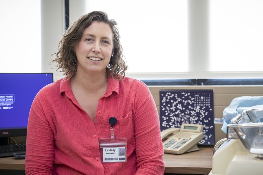 Lindsay MacDougall is pictured inside the Well Newborn and Parent Clinic, located at Kingston General Hospital. She has short, medium brown, wavy hair and blue eyes. She's wearing a bright pink, button down blouse.